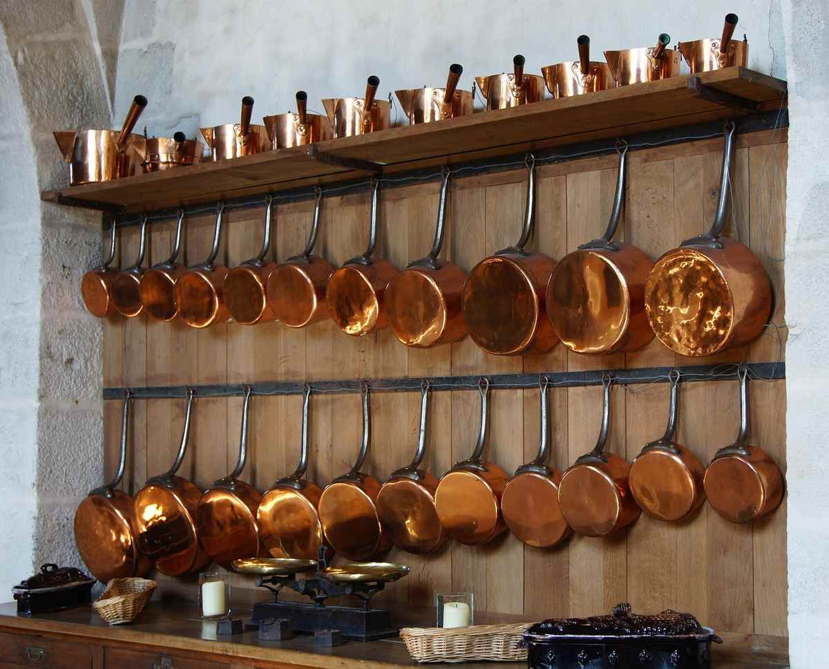 Cuisines en cuivre suspendues sur des étagères en bois contre un mur de pierre Cuisines en cuivre suspendues sur des étagères en bois contre un mur de pierre
