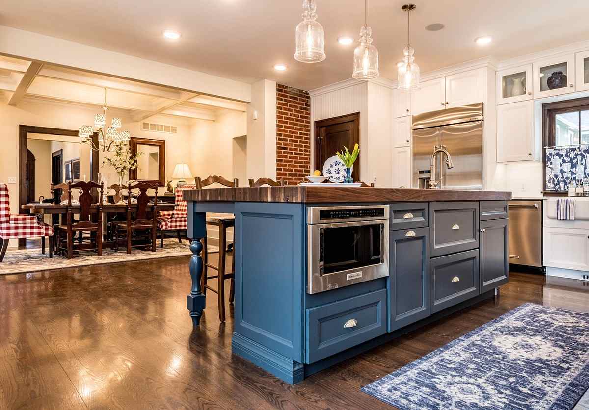 Cuisine moderne avec îlot bleu, four intégré, chaises rouges, lampe suspendue, sol en bois
