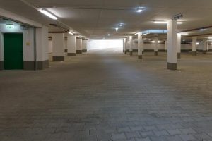 Parking souterrain désert, colonnes, sol pavé, porte verte, lumière