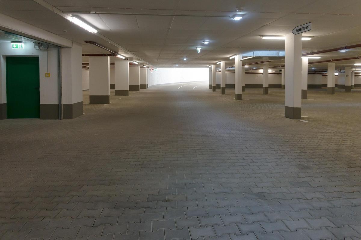 Parking souterrain désert, colonnes, sol pavé, porte verte, lumière