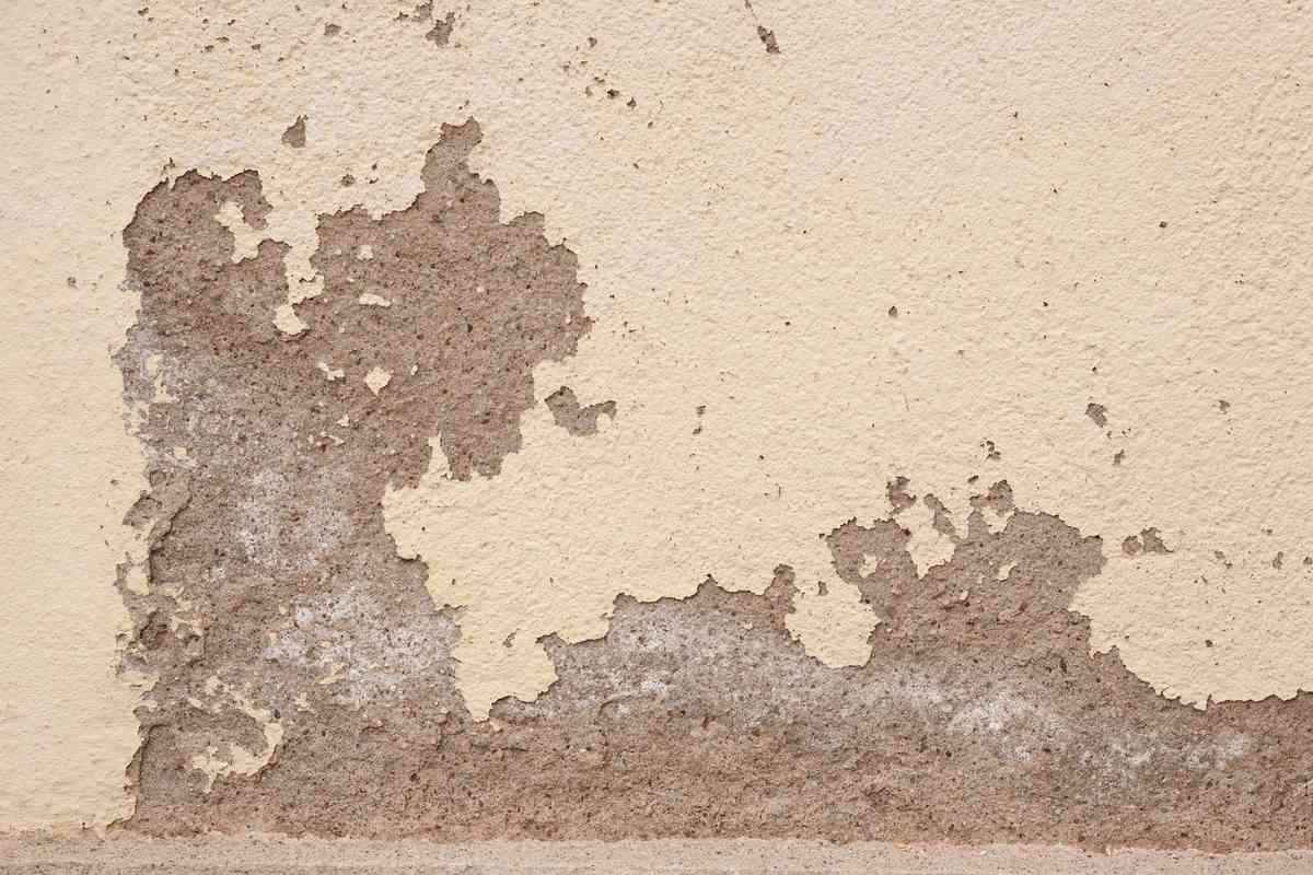 Enduit qui s'écaille sur un mur beige révélant la couche grise Enduit qui s'écaille sur un mur beige révélant la couche grise