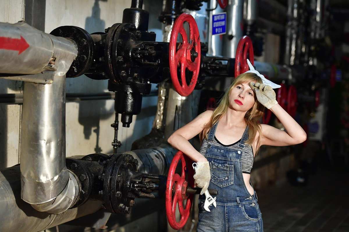 Femme en overalls devant tuyaux et manivelles rouges, pose contemplative Femme en overalls devant tuyaux et manivelles rouges, pose contemplative