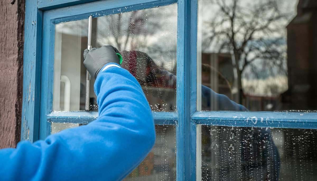 Une personne en gants bleus nettoie une fenêtre en bois