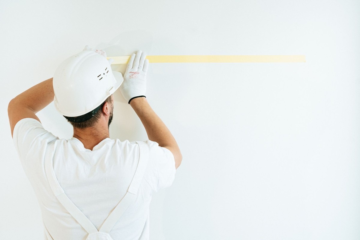 Un ouvrier en tenue blanche mesure un mur blanc avec un ruban Un ouvrier en tenue blanche mesure un mur blanc avec un ruban