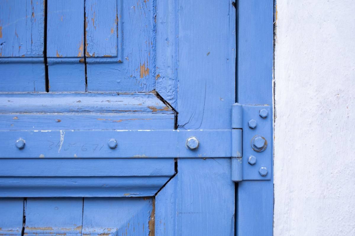 Porte bleue usée avec charnière, cadre en bois, mur blanc à droite Porte bleue usée avec charnière, cadre en bois, mur blanc à droite